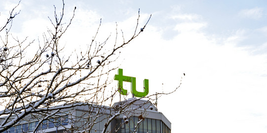 Ein Gebäude mit TU Dortmund Logo und mit Schnee bedeckte Äste.